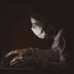 A woman wearing a mask looking at her laptop