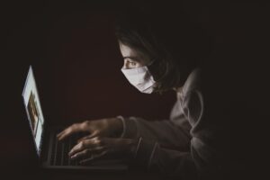 A woman wearing a mask looking at her laptop